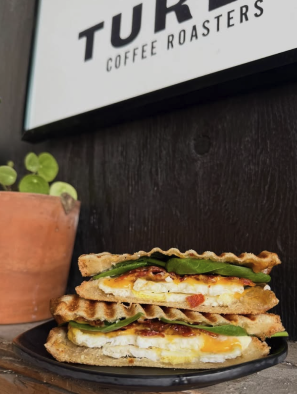 Grilled breakfast sandwich with eggs, melted cheese, bacon, and spinach served on a black plate at Turbo Coffee Roasters in Huntsville.