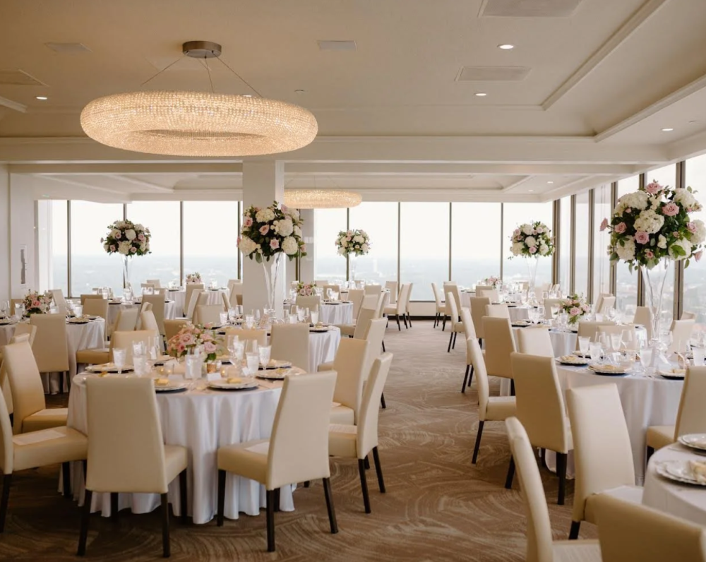 The interior of the top floor at La Vetta with large bright windows and tables with white table cloths, white chairs, and white and green floral arrangements.