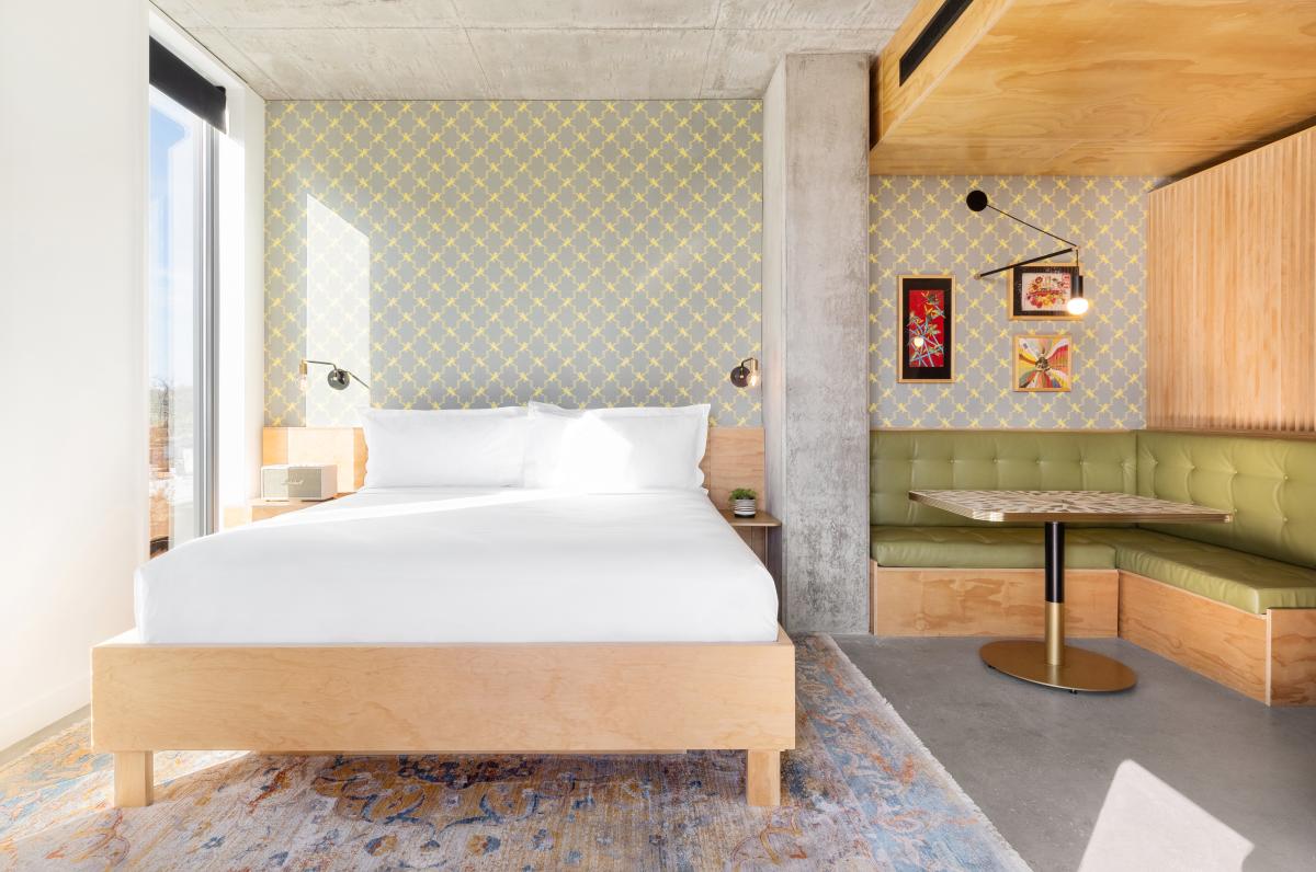 A bright and neutral colored hotel room at ARRIVE Austin featuring a white bed and a sitting table.