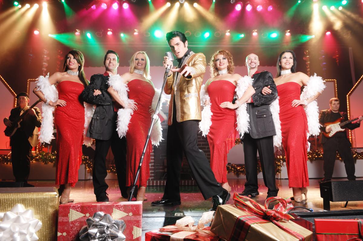 An Elvis impersonator stands on stage in front of a line of four women and two men during Legends in Concert