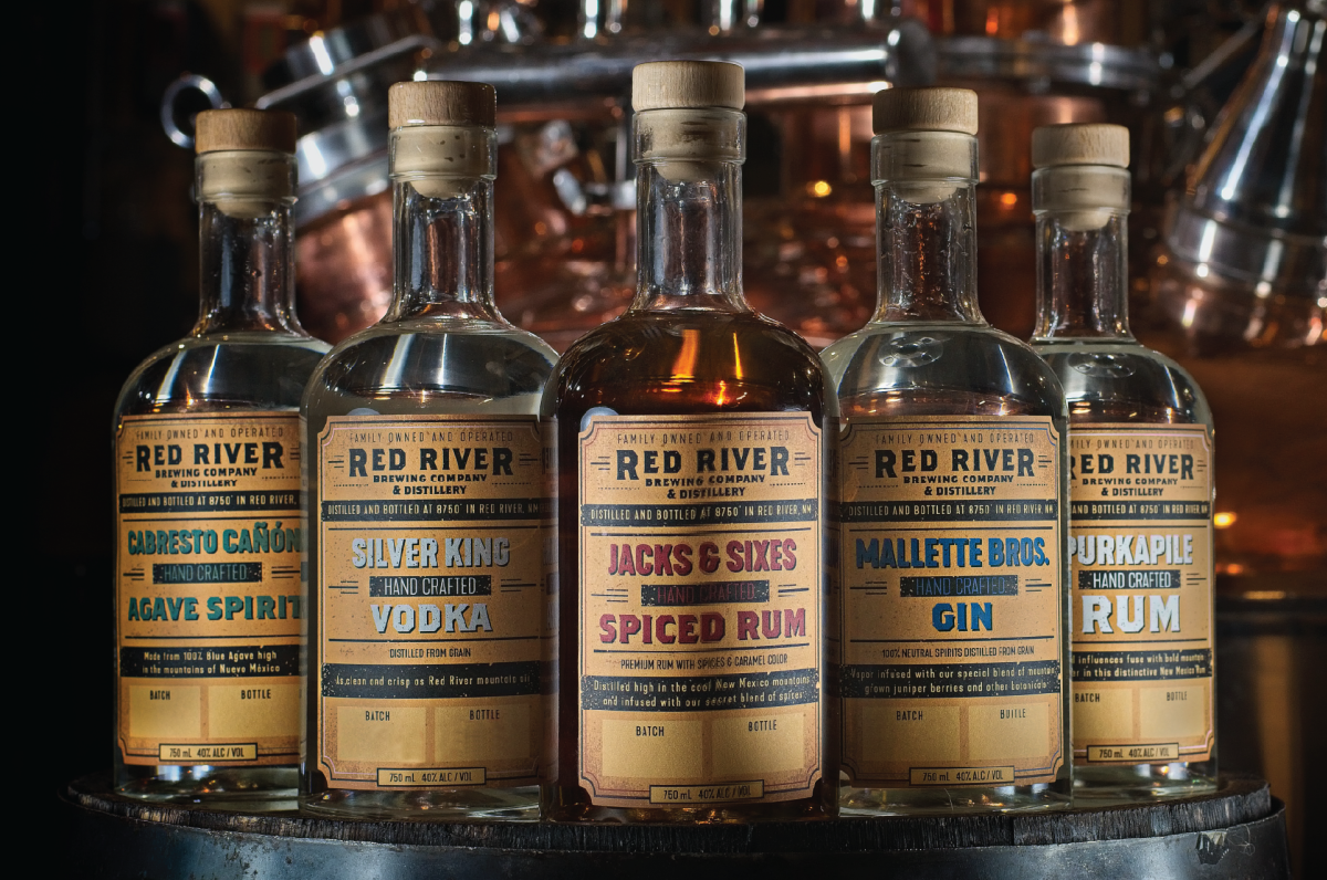Bottles of Red River spirits arranged in a row against copper distillery equipment.