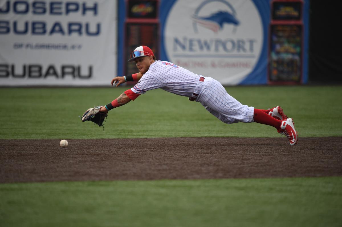 A baseball player is extended midair horizontally to catch a ball.