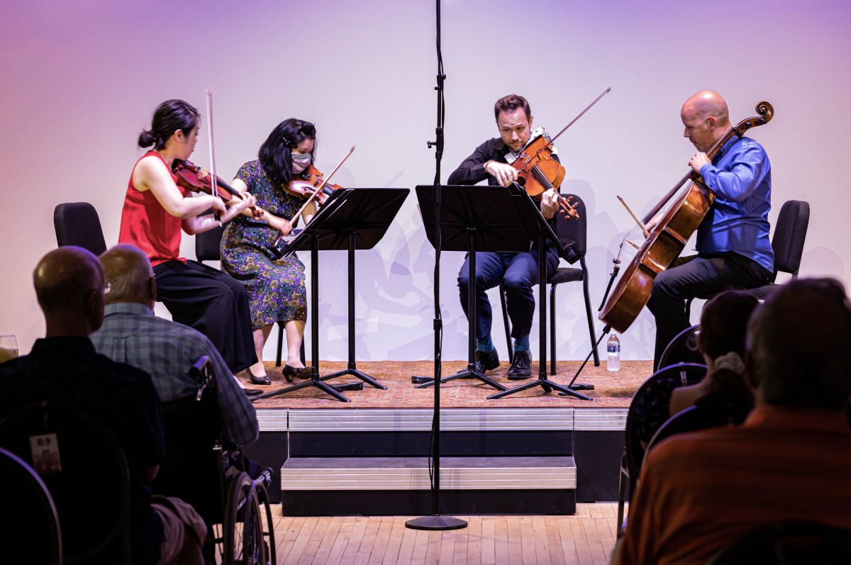 Four musicians performing in a string quartet on stage at The Block in downtown Muskegon in front of an audience.