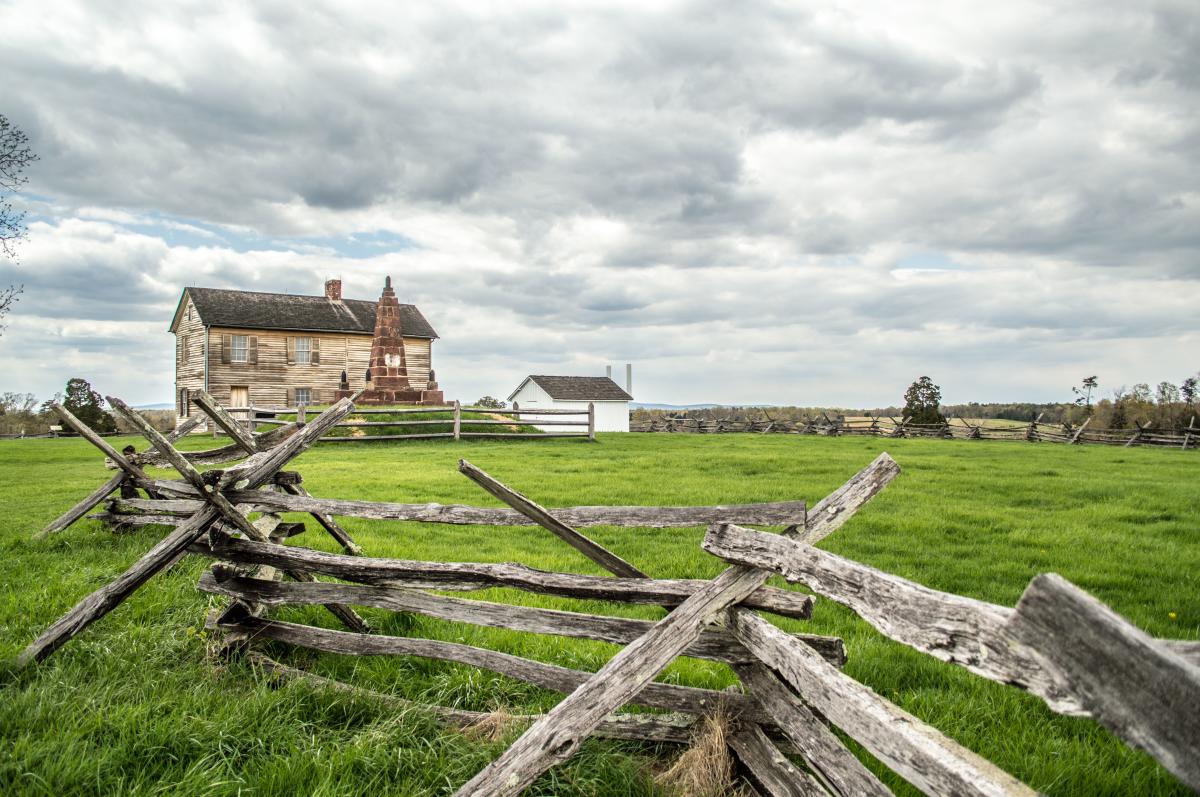 A battlefield with a wooden fence and a historic building in the background