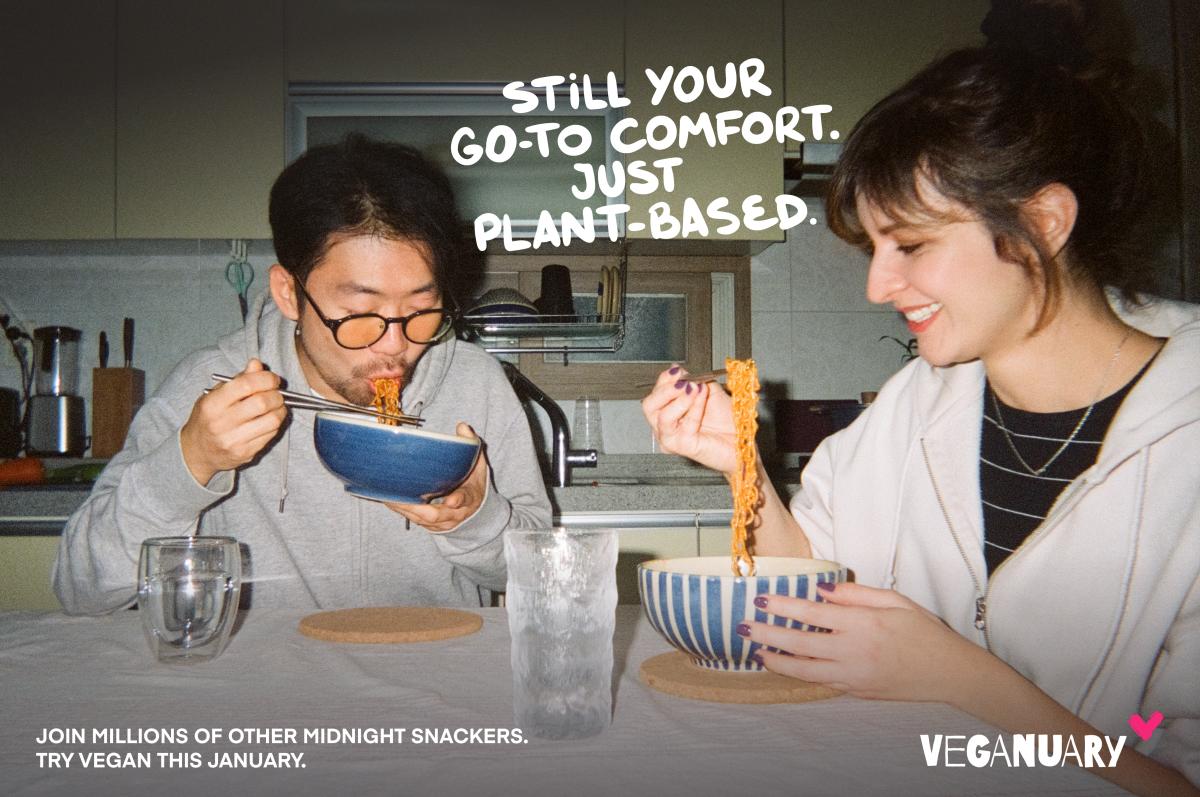 Woman and man sitting at kitchen table eating noodles with text overhead saying 'still your go-to comfort. Just plant based'