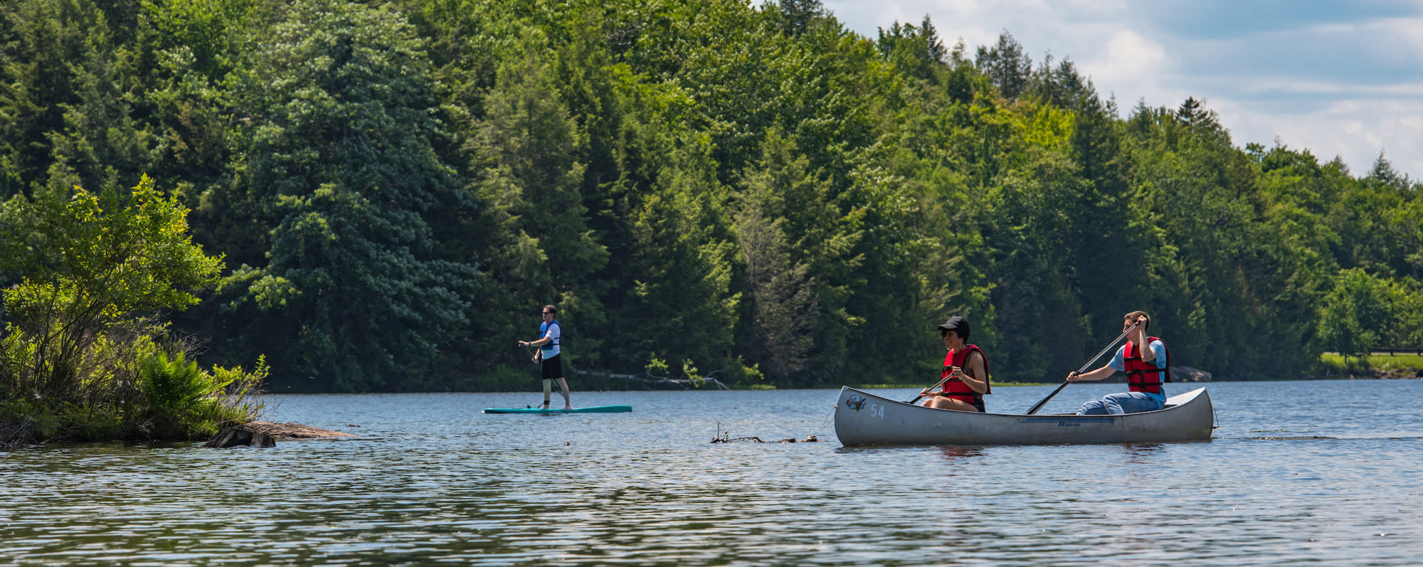 A photo of two people in a canoe and one person paddle boarding on a lake on Noth-South Lake Campground