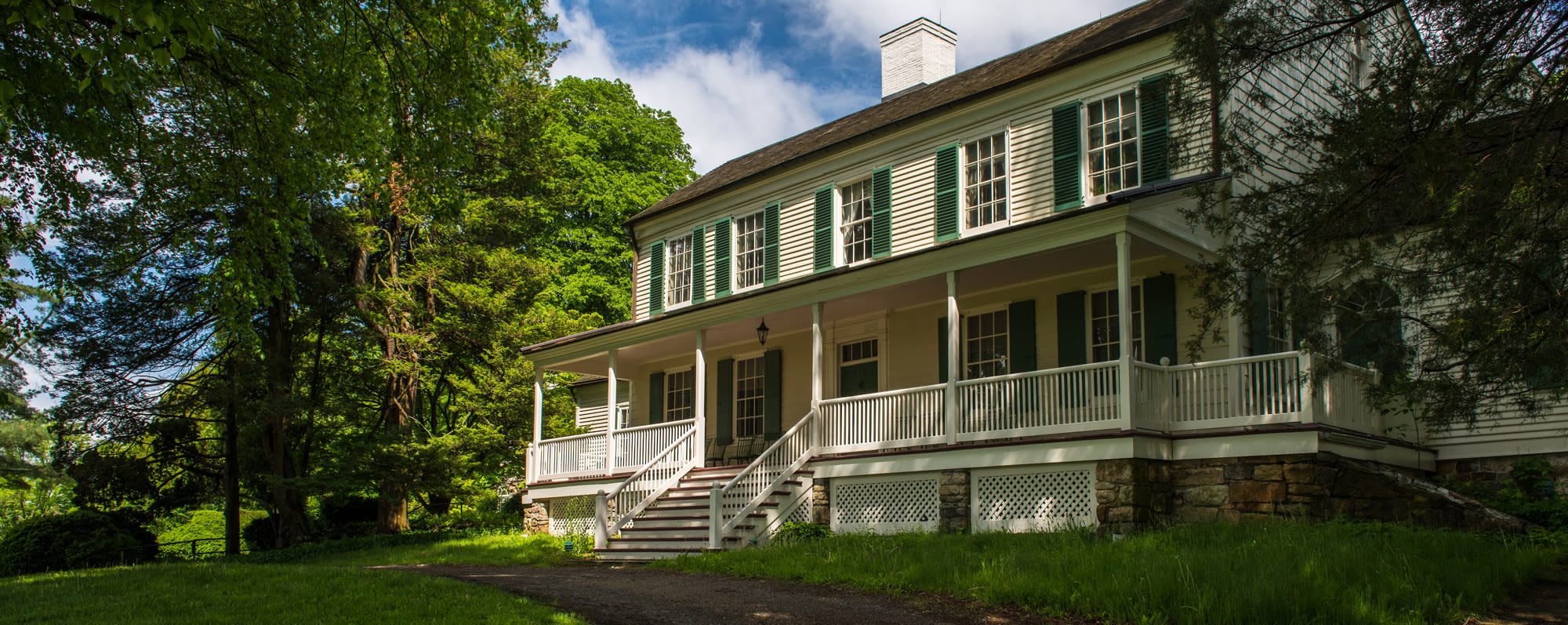 The exterior of John Jay Homestead State Historical Site on a sunny day with green foliage