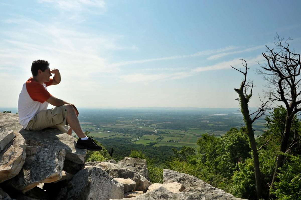 Hiker sitting on a rock and shading his eyes with his hand to overlook the view on Waggoners Gap