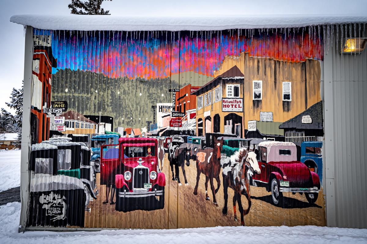 A mural of a street with horses and old cars on it