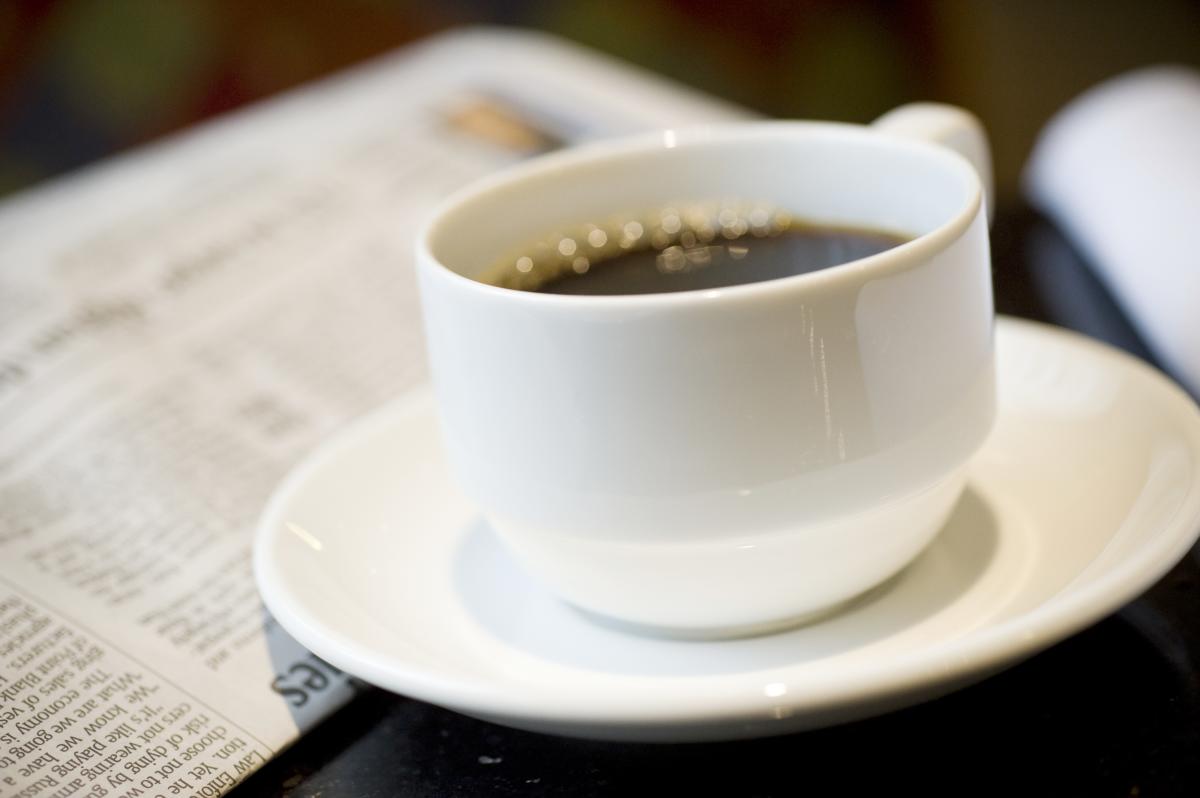 Coffee cup on saucer sits next to a newspaper on a table