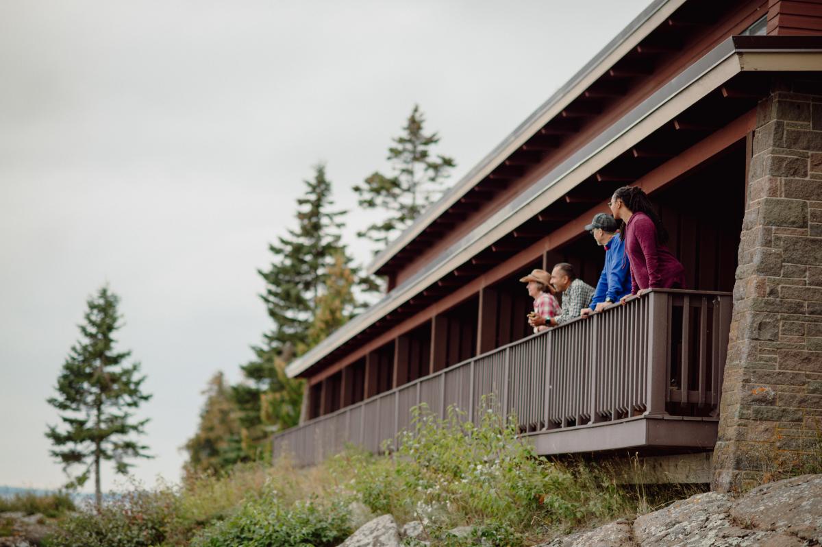 four people lean on the railing of a lodging porch
