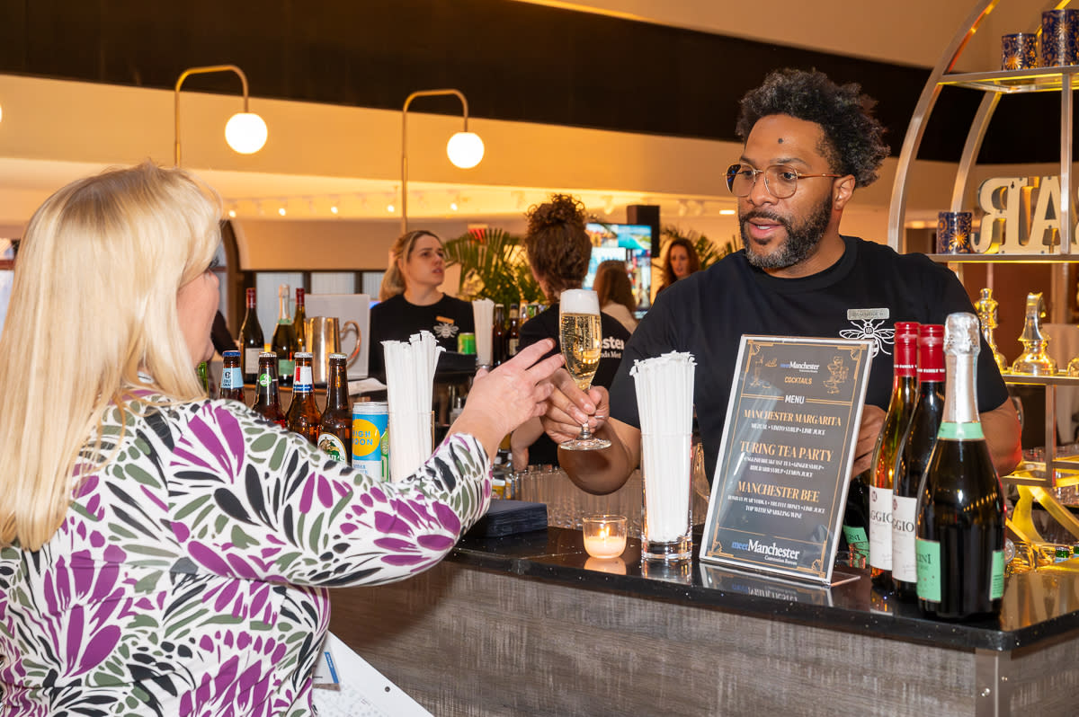 A barman hands a glass of wine to a conference delegate