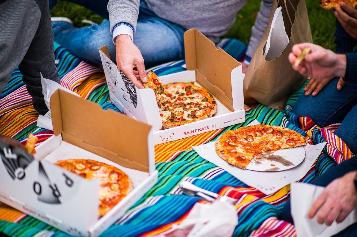 Three people eating personal pizzas outside on a colorful picnic blanket