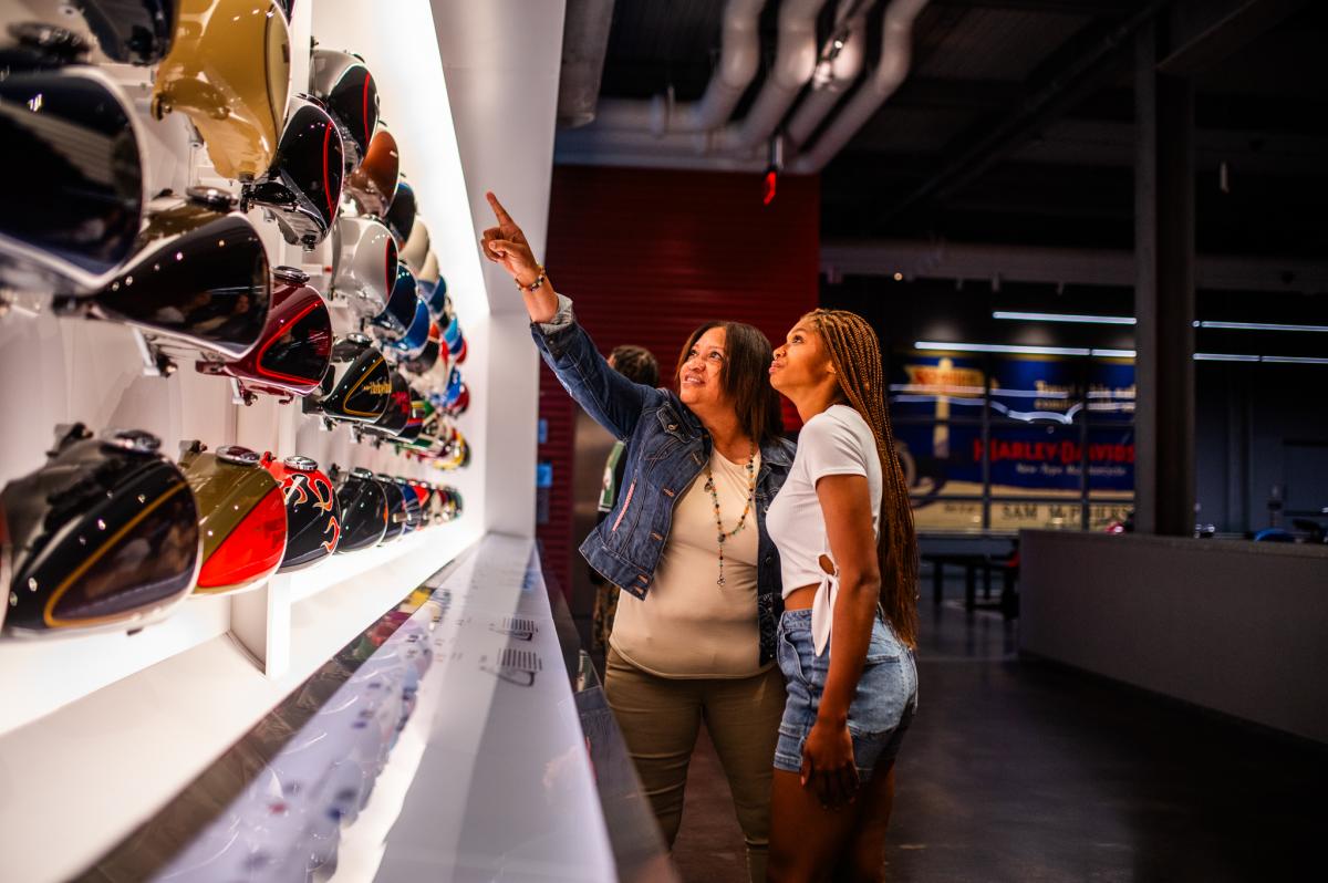 a mother and daughter pointing at a wall of motorcycle tanks