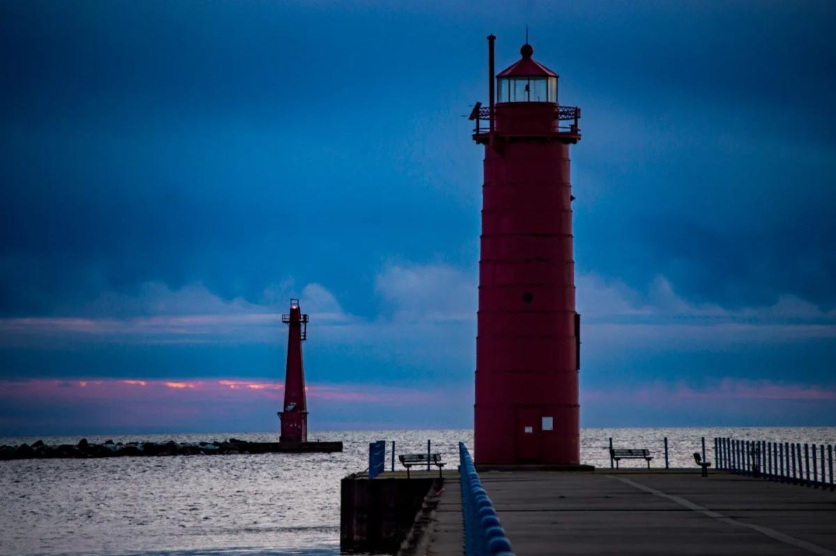 Sunset at Muskegon South Pierhead Light with vibrant blue skies and soft pink horizon in the background, featuring two red lighthouses on a pier at Pere Marquette Park in Muskegon, Michigan