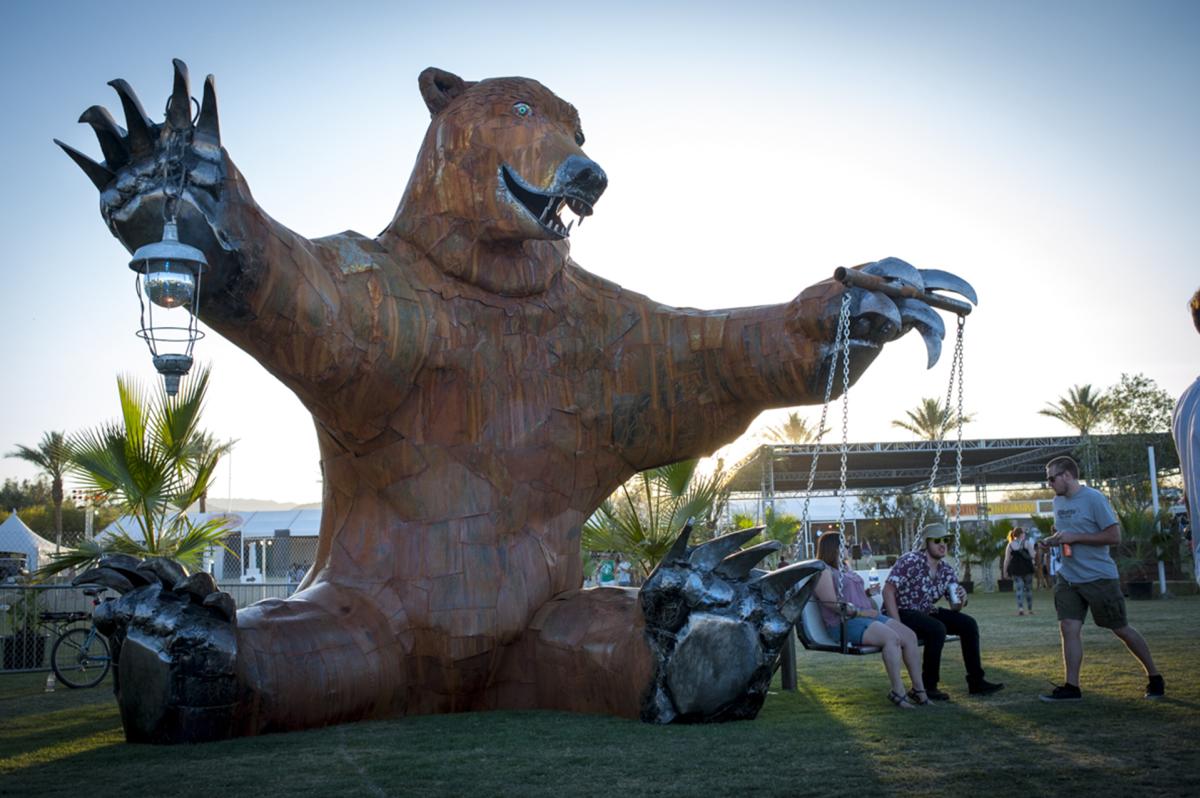 A 24-foot tall bear sculpture sits on the Coachella Festival grounds holding a custom porch swing from its left paw and a disco ball in its right.