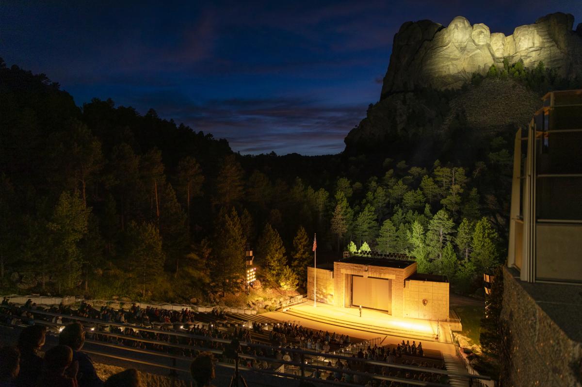Audience at night watching Mount Rushmore Lighting Ceremony with Mount Rushmore lit.