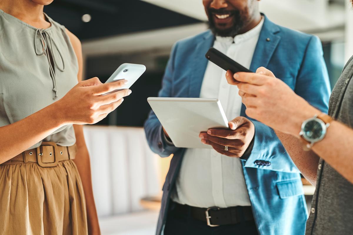 Three people look at their mobile phones and tablets while strategizing a digital services campaign.