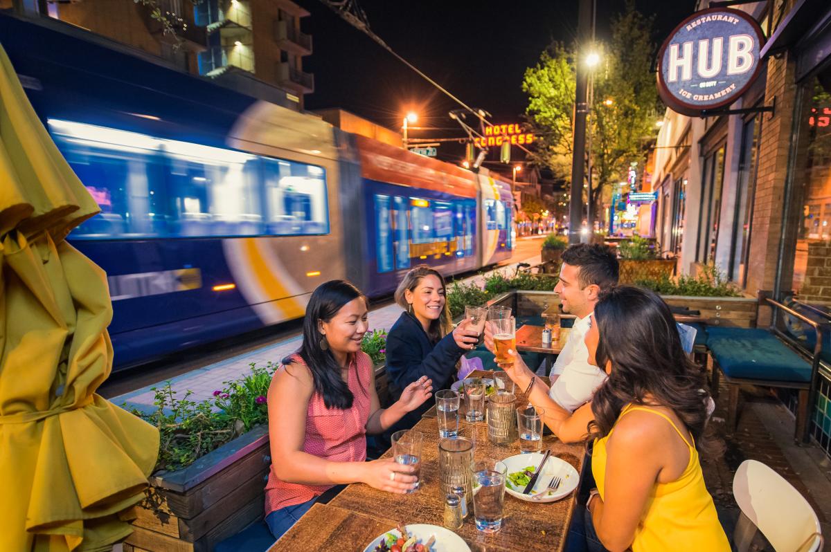 Three women and one man dining outdoors at Hub Restaurant downtown at night