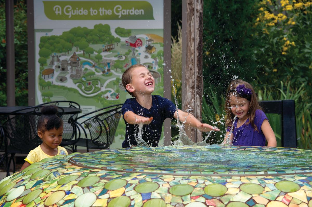 Three kids play in a water feature at a garden in Botanica Wichita