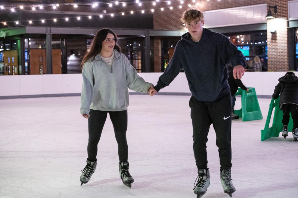 A teen boy and girl hold hands while ice skating at Chicken N Pickle.