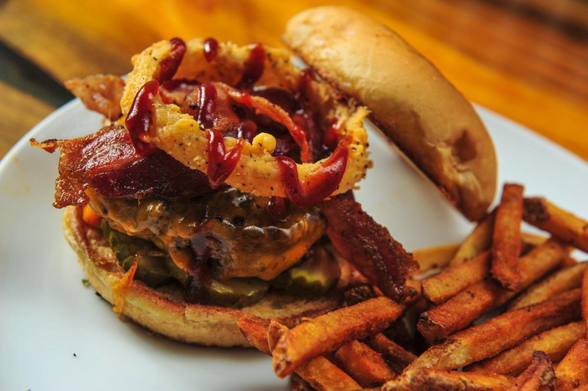 A cheeseburger topped with barbeque sauce bacon and onion rings is served with a side of fries at The Rusty Nail