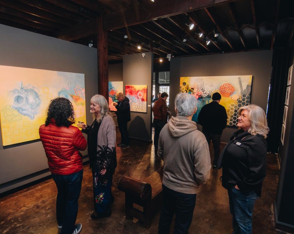 A group of men and women chatting in a dark gallery during an exhibition open at Davis Gallery.