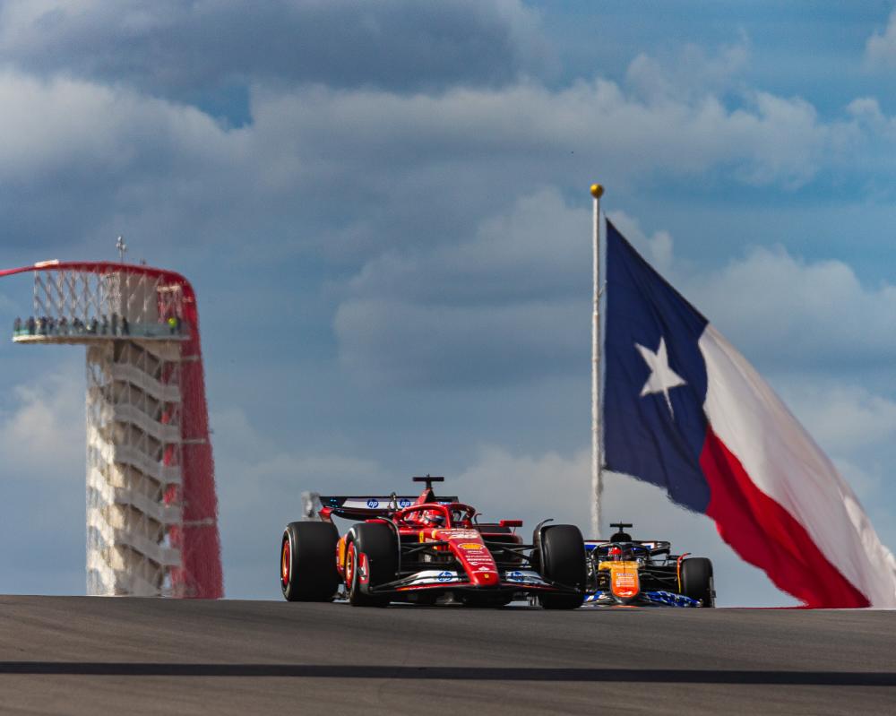 Image of a formula 1 car on the track at Circuit of the Americas with the tower and a large Texas flag in the background.