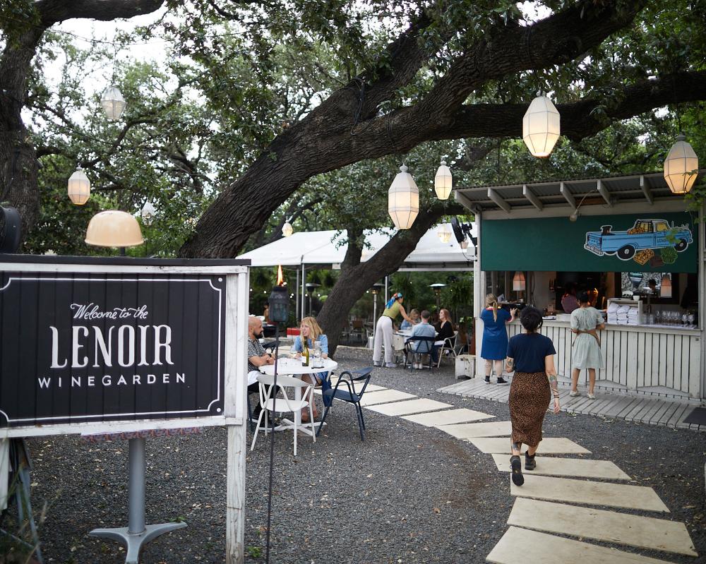 Image of the entrance at Lenoir with outdoor seating and lanterns hanging overhead from a large oak tree.