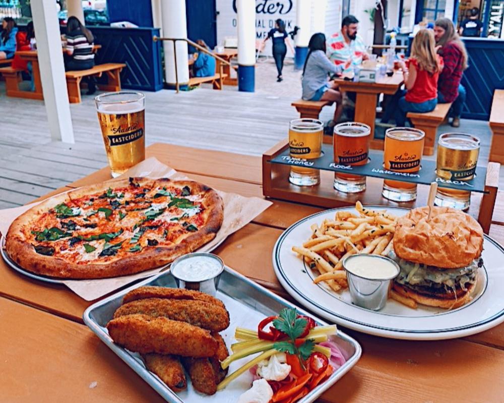 Pizza, fried jalapenos and burger sitting on a table with a colorful flight of Austin Eastciders ciders.