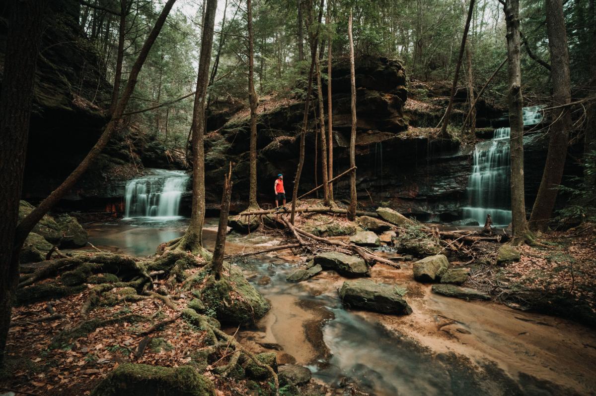 A guy in Bankhead forest standing in between two waterfalls.