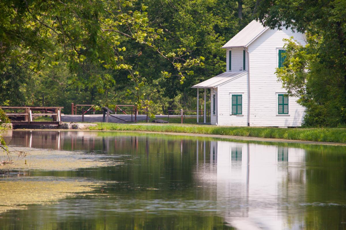 Historic white lock house and Canal Lock 70 reflected in Battie Mixon Fishing Pond along the C&O Canal in Oldtown, Maryland