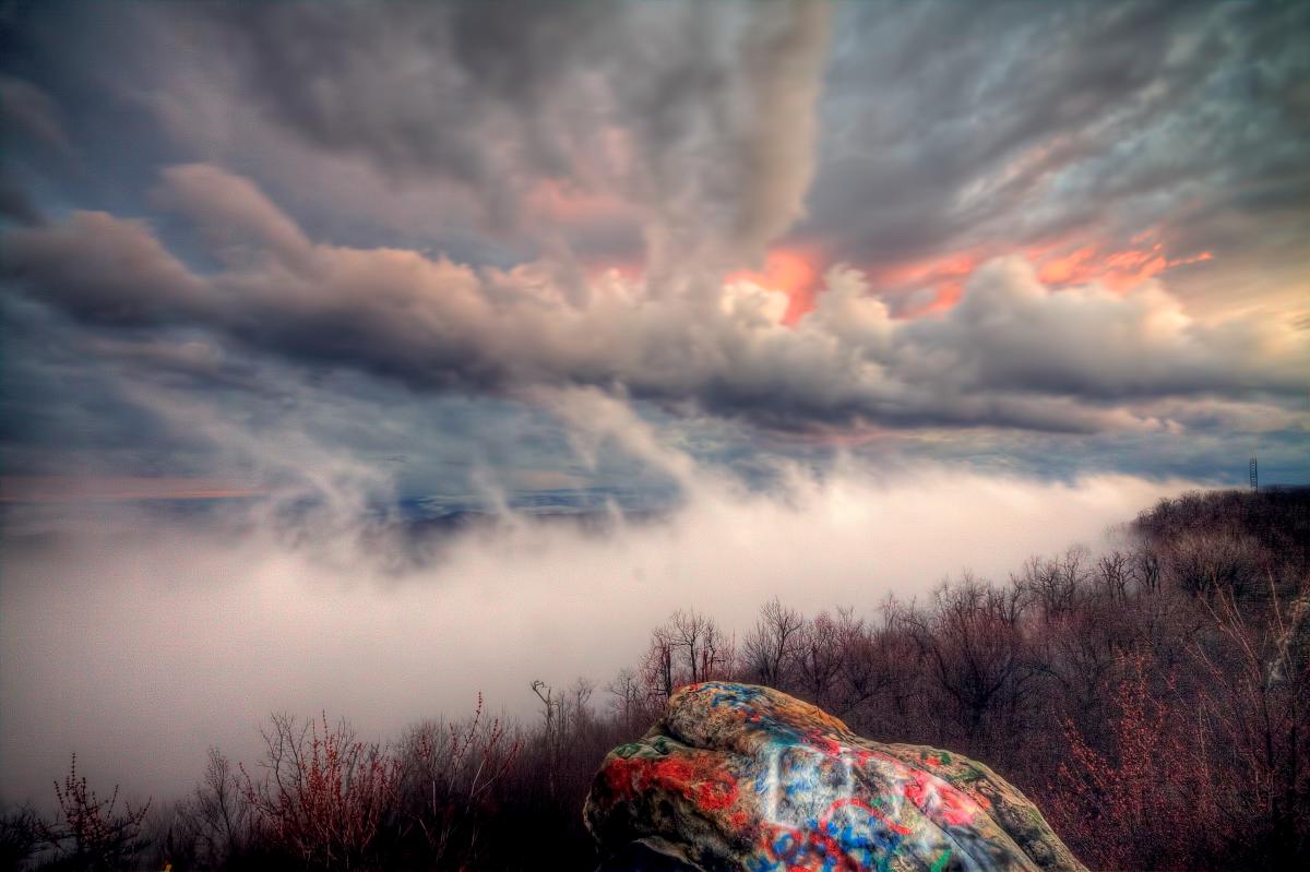 Mist rises from the mountain overlook with clouds forming and peaks of pink sunrise poking through.