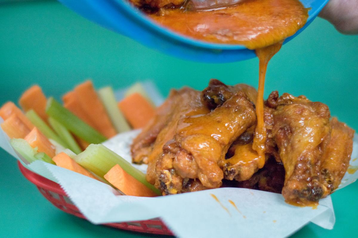 Basket of wings with buffalo sauce being poured over them.