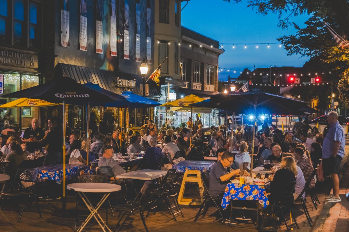 String lights over a crowd of people eating dinner under the stars on west street.