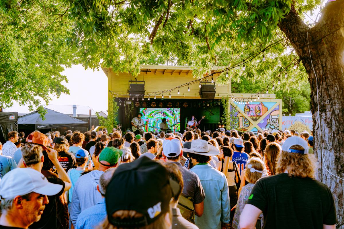 Image of a band performing on a small yellow framed stage with a large group of people standing in front of the stage.