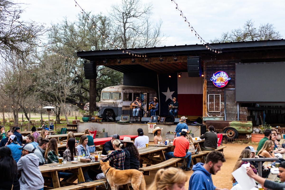 People sitting outside at picnic tables with a band onstage in the background at Armadillo Den.