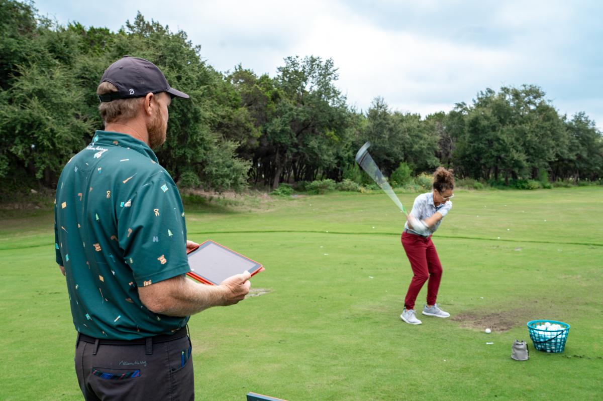 A woman swinging a golf club as a man stands behind her watching.
