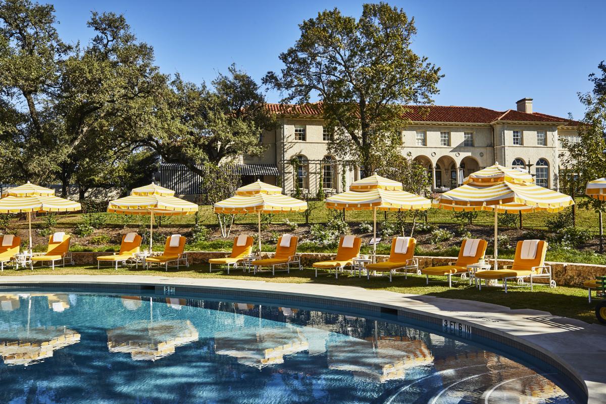 The pool at Commodore Perry Estate surrounded by yellow lounge chairs and umbrellas with the hotel in the background.