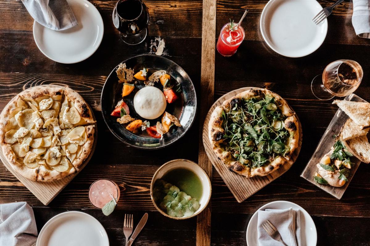 Lay flat image of a table at Intero with drinks, pizzas, and pasta in dishes on the table.