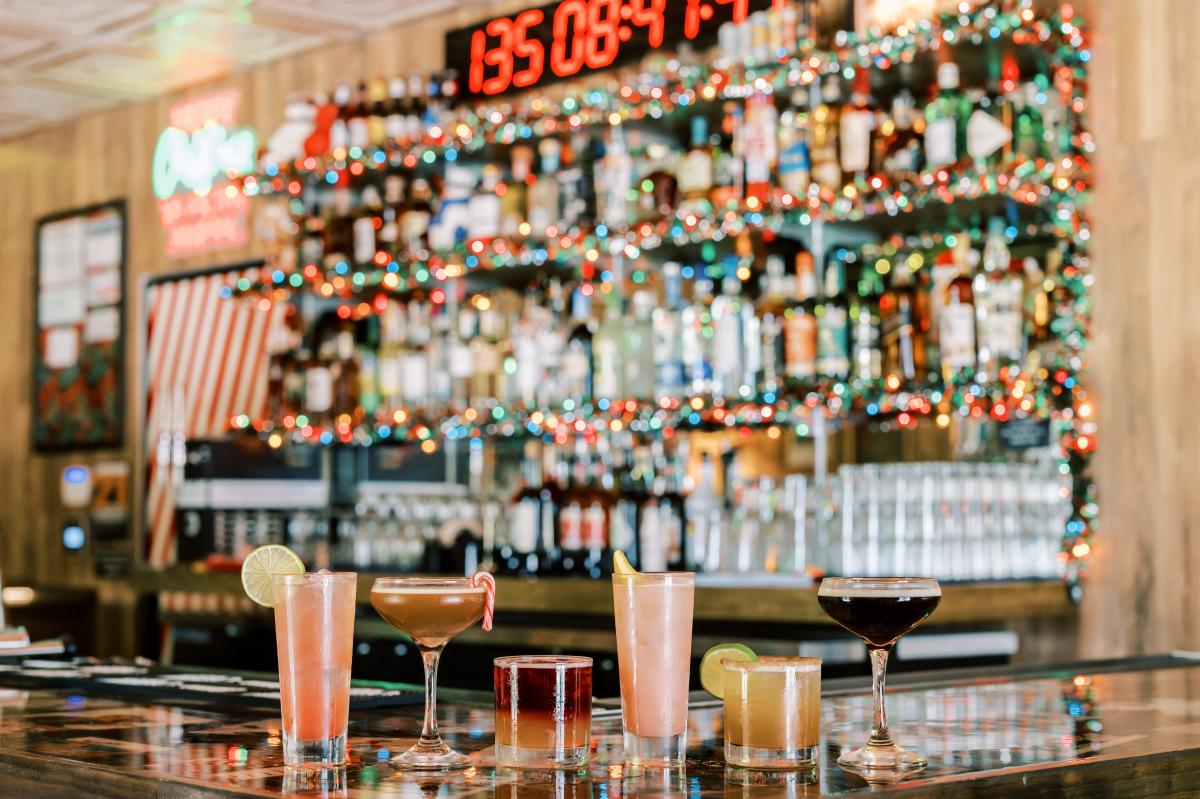 Image of several different style cocktails sitting on the bar with festive colorful lights in the background at Lala's Little Nugget South.