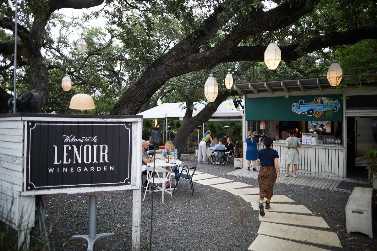 Image of the entrance at Lenoir with outdoor seating and lanterns hanging overhead from a large oak tree.