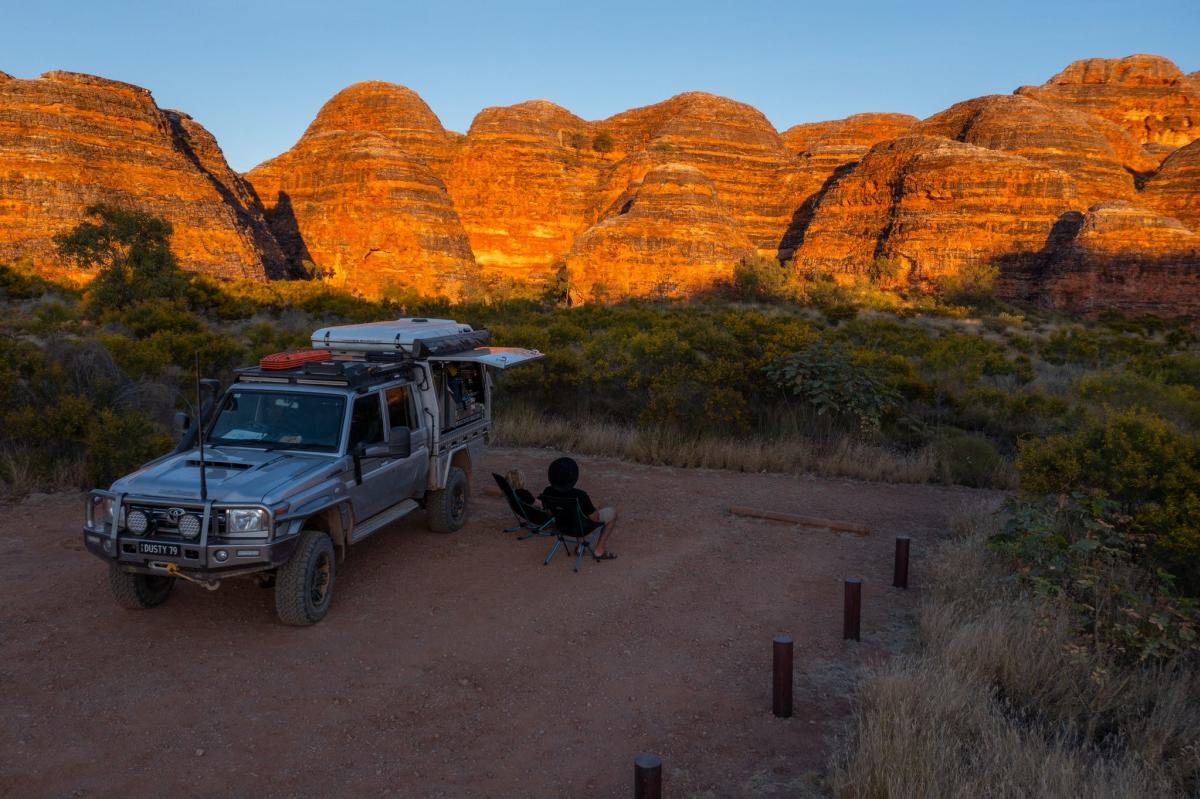A man sits alongside is 4WD at a car park in Purnululu National Park. He's watching the sunset over the striped domes of the Bungle Bungle Range.