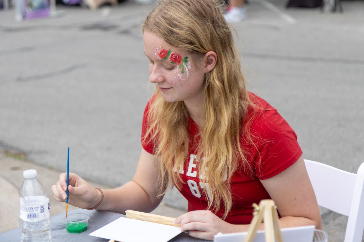 F.A.M.E. attendee painting on a canvas at the Bastrop Cultural Arts Committee table as part of the event.