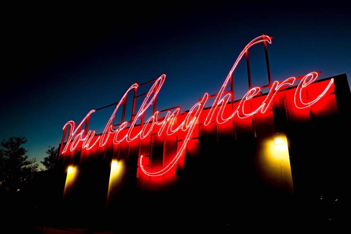 Neon sign reading "You Belong Here" illuminated against a twilight sky, creating a welcoming atmosphere for visitors.