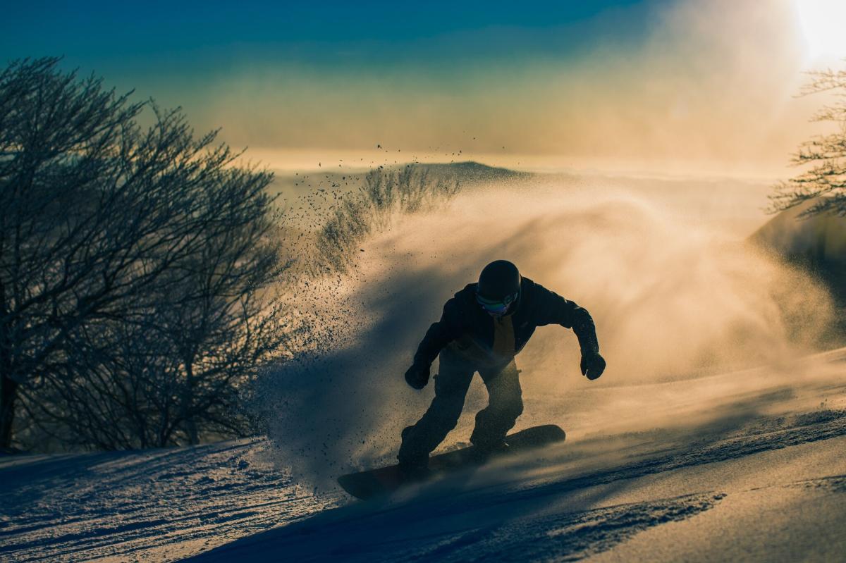 Someone snowboards down a slope with a huge spray of snow behind them.