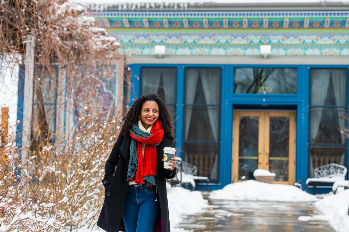 A person smiling and holding a warm drink outside the Boulder Dushanbe Teahouse.