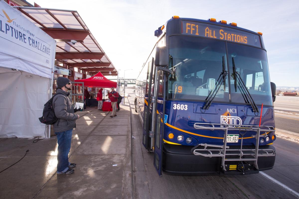 An RTD Flatiron Flyer bus waits at a station as a passenger stands nearby.