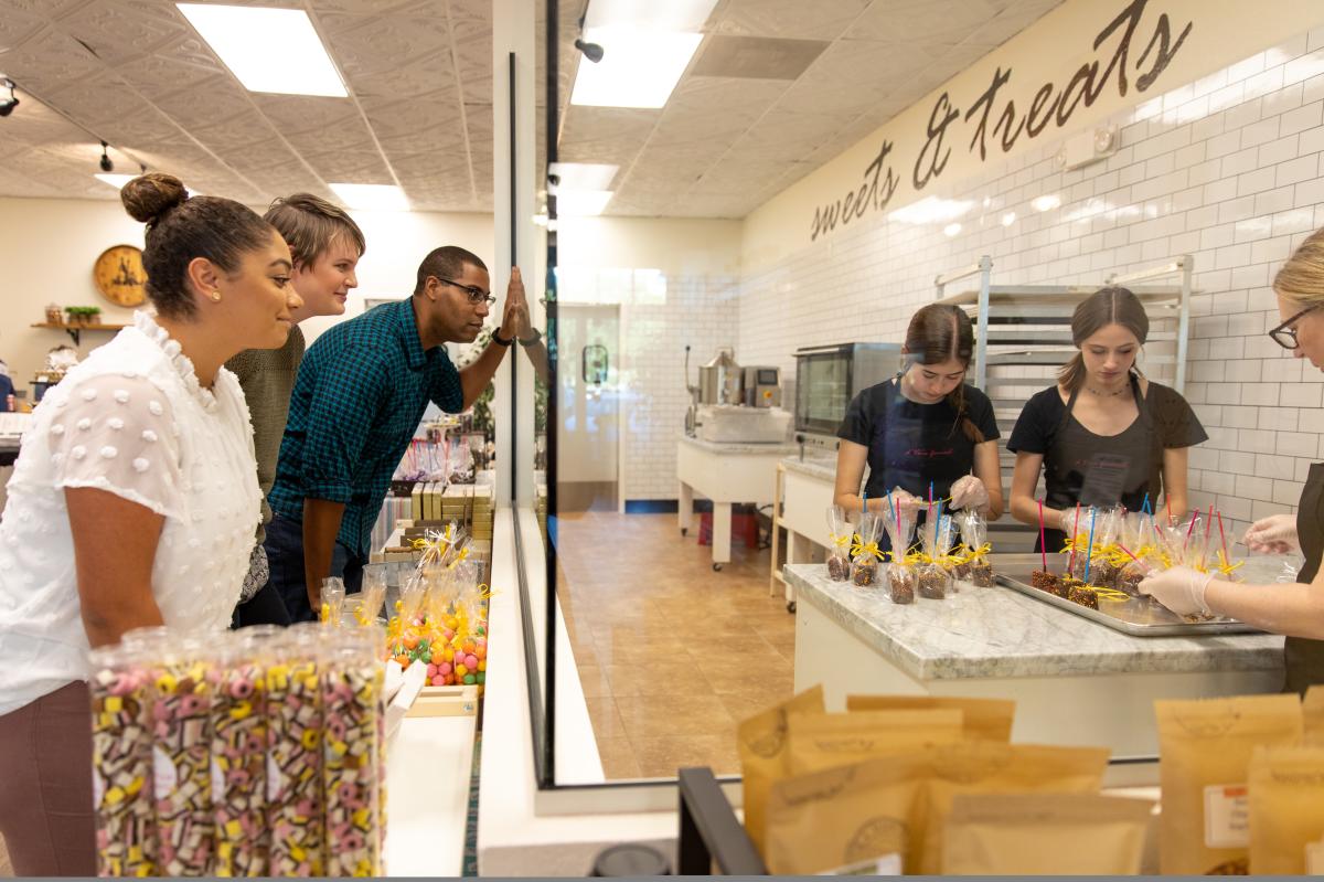 a group of friends watching the store staff make homemade candy through a glass window