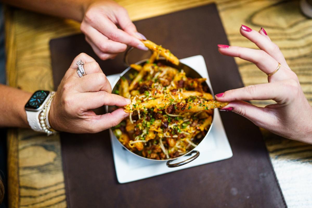 three different hands pulling duck fat French fries from a bowl